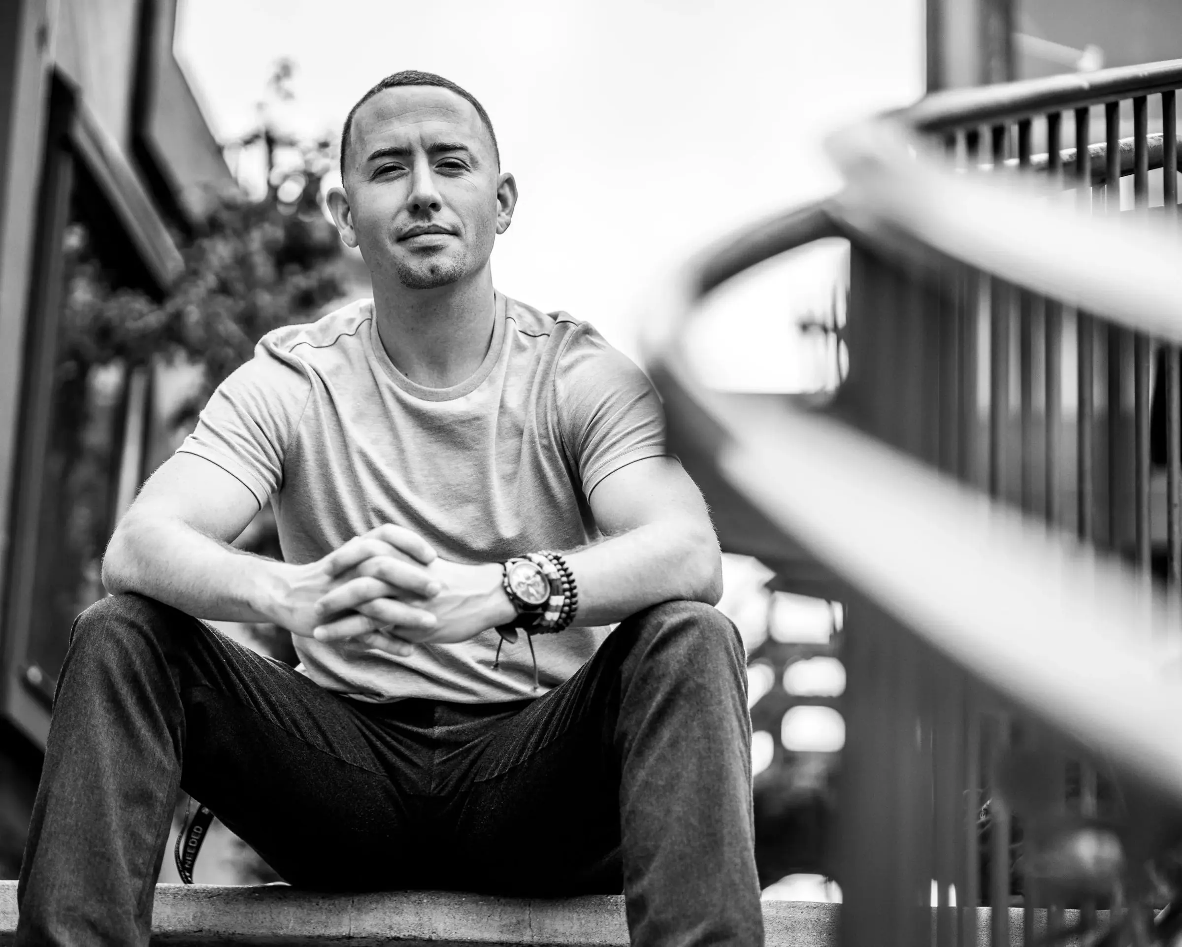 Black-and-white portrait of a man sitting on steps, hands clasped