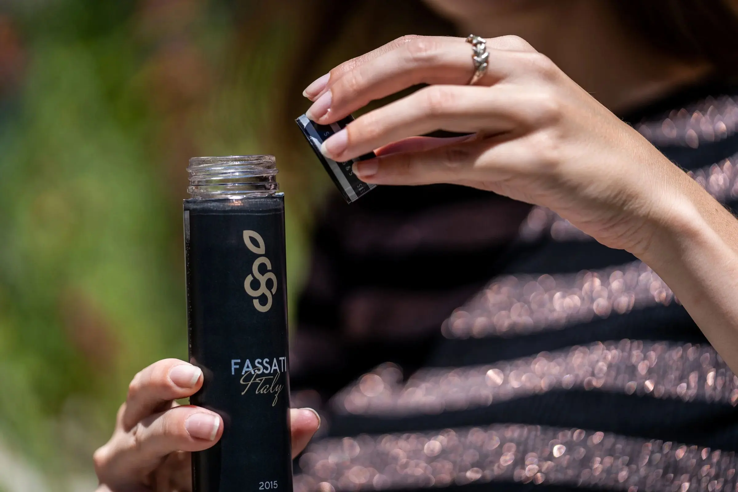 A hand tilting a dark wine bottle against sequined fabric